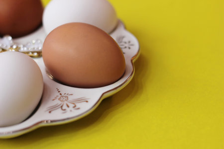 White and brown eggs lie on a special plate on a yellow background. Preparation for Easter. Diet and...