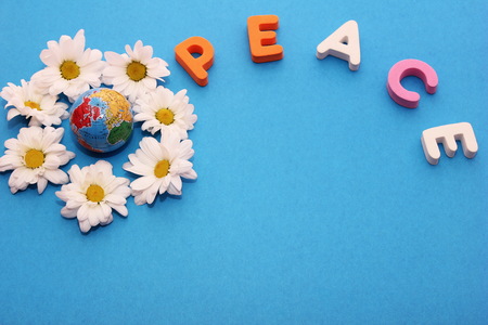 Word PEACE made by letters near little figure of a globe surrounded by flowers of white chrysanthemums. Blue background and empty space to insert text.の写真素材
