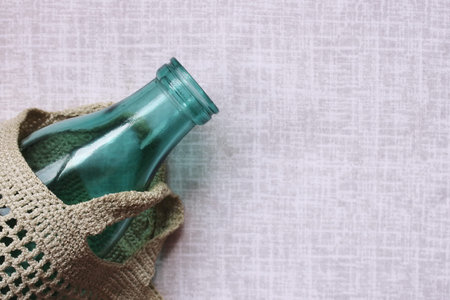 The glass bottle is in a knitted bag on the linen tablecloth. Reusable packaging. The concept of environmental protection.Empty space for text.の写真素材