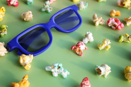 Glasses in blue plastic frame to watch the movie in 3D format among colored popcorn and candy on a green background.の写真素材