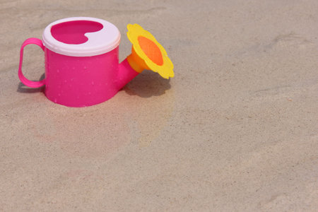Toy pink watering can with a lid in the shape of a heart is located on the wet sand of the sea coast on a Sunny summer day.の写真素材