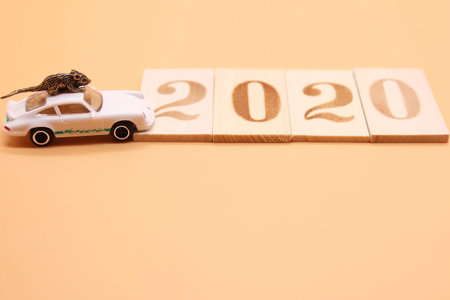 A toy little rat on the roof of a toy car next to the 2020 wooden figurines. Copy space.