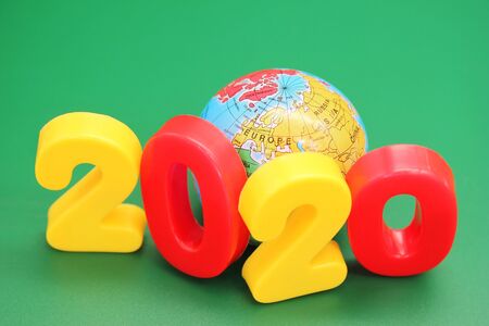 2020 new year's number next to the toy globe on a green background.の写真素材