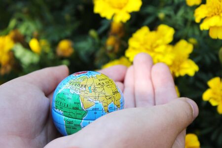 the child holds the planet Earth in his hands on a background of flowers . Earth day. The green concept. A toy globe in childrens hands. the concept of Earth Dayの写真素材