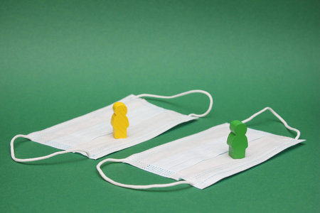 Quarantine. Wooden figures of people stand on medical masks. Green background. COVID-19 danger....