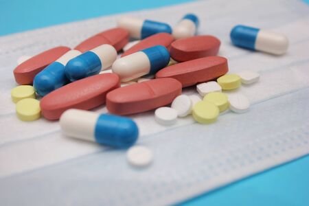 A medical mask and a lot of pills and pills around on it on a blueの写真素材