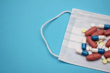 A medical mask and a lot of pills and pills around on it on a blue background. Concept of a coronavirus pandemic. Quarantine and travel ban. COVID-19 danger.の写真素材