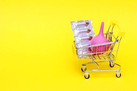 Medical suppositories in a silver blister pack and a pink rubber medical enema are placed in a toy shopping cart. Packaging of contraceptives, vaginal, rectal candles. New pink medical enema.の写真素材