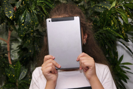 The girl holds a digital tablet in front of her face. To spoil your eyesight. Harm to the view from the gadget .の写真素材