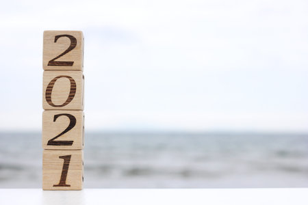 Wooden blocks with the numbers 2021 stand on top of each other like a pyramid near the sea. Happy...