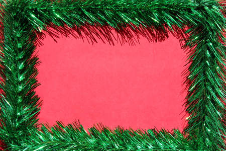 Christmas frame made of green tinsel on a red background. Copy space. Empty space for text. Blank for an online Christmas card.の写真素材
