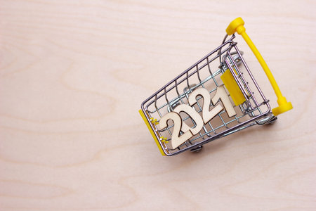 The numbers 2021 in a supermarket toy cart on a wooden background. Happy New year. Shopping concept.