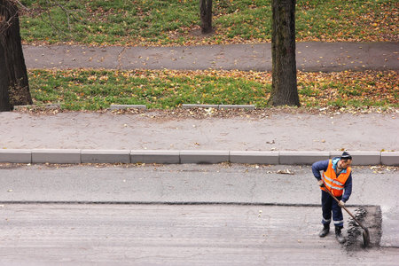 Russia, Vladivostok October 21, 2020: A road worker in an orange vest removes old asphalt with a...