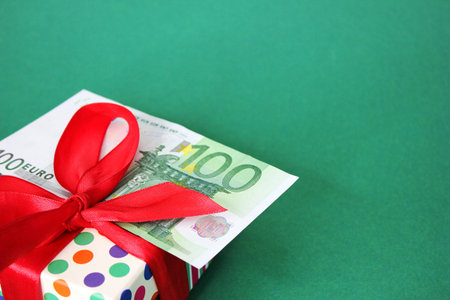 100 Euro banknote on a gift box with a red bow. Green background. The concept of a holiday and cash gifts.の写真素材