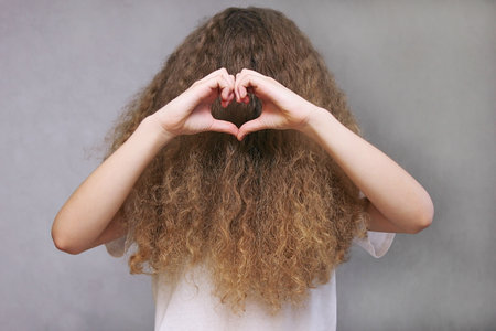The girl pushes back her thick wavy hair and shows the shape of a heart with her fingers. The magic of womens hair.の写真素材