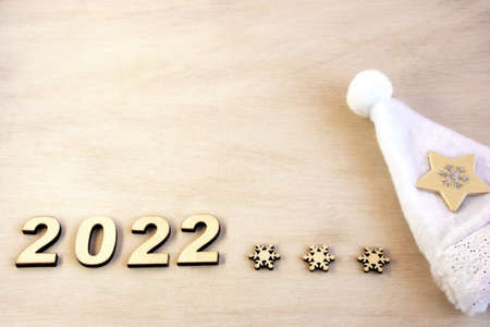 New year number 2022 lined with wooden figures on the wooden surface next to the white Christmas hat. Happy New Year.の写真素材