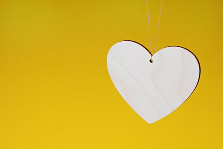 A wooden heart is hanging on a string on a yellow background.の写真素材