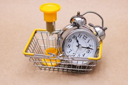 An hourglass and a metal alarm clock in the shopping basket. The concept of time.
