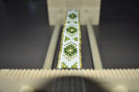 A close-up of hands crafting a beaded bracelet on a specialized loom. The bracelet features a traditional pattern with colorful beadsの写真素材