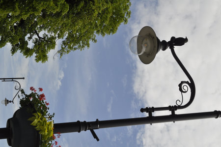 Lamppost on blue sky background with white clouds and green leavesの写真素材