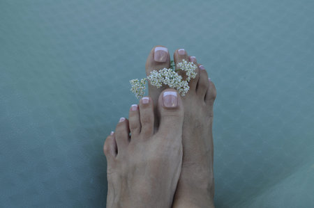 Female feet with beautiful pedicure and flowers on a green background