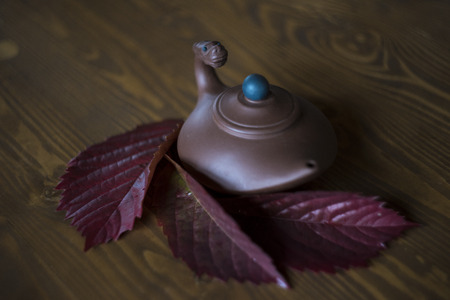 Teapot with red grape leaves on dark wooden backgroundの写真素材