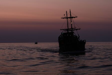 Two silhouettes of ships floating on the sea against the darkening skyの写真素材