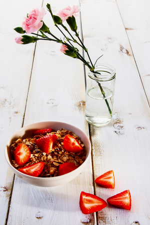 Bowl of healthy breakfast cereal topped with fresh strawberries over white wooden table.の写真素材