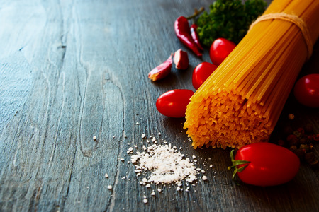 Whole wheat spaghetti and tomatoes with herbs on wooden texture. Selective focus.の写真素材