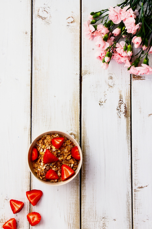 Bowl with cereals and strawberries for breakfast on white wooden table. Top view.の写真素材