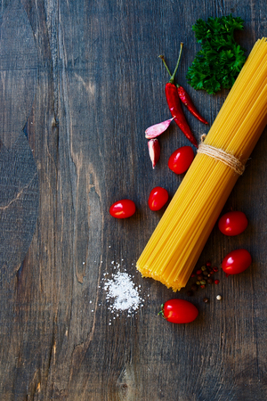 Top view of spaghetti and tomatoes with herbs over rustic and vintage wooden texture.の写真素材