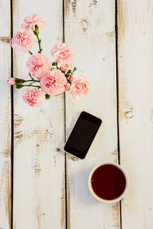 Smartphone, cup of coffee and flowers on white wooden backgroundの写真素材