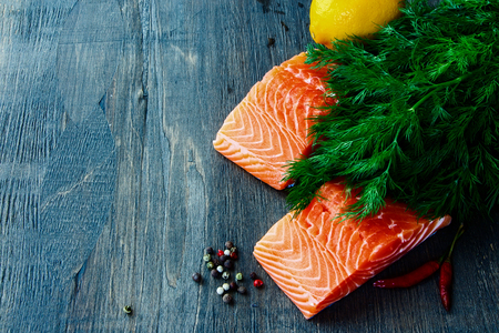 Fresh salmon fillet with aromatic herbs and spices over dark wooden textureの写真素材