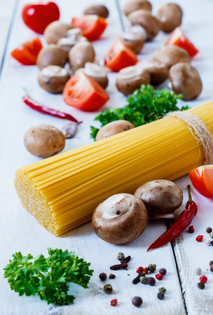 Italian food. Pasta with tomatoes, mushrooms, herbs and spices on white wooden background with space for textの写真素材