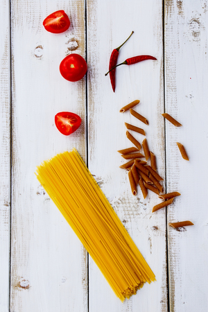 Whole wheat pasta with tomatoes on white wooden background. Top view.の写真素材