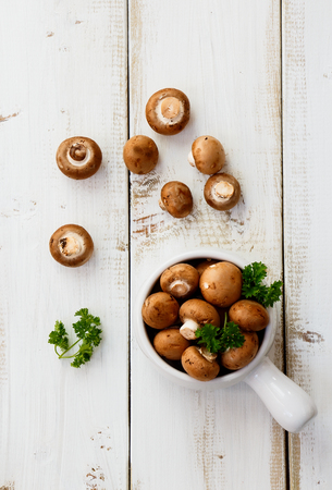 Fresh brown mushrooms with herbs on white wooden background. Top view.の写真素材