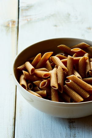 Ceramic bowl with whole wheat pasta on white wooden background. Selective focus.の写真素材