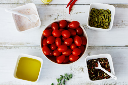 Cherry tomatoes with herbs, spices, olive oil, pink salt and lemons on white wooden board. Top view.の写真素材
