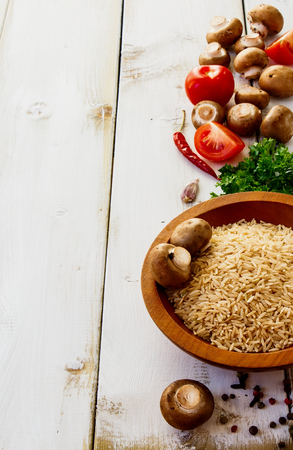 Ingredients rice, mushrooms, tomatoes, herbs and spices for cooking over white wooden backgroundの写真素材