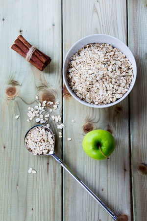 Diet breakfast - bowls of oat flake, apple and cinnamon on wooden background - health and diet concept. Top view.の写真素材