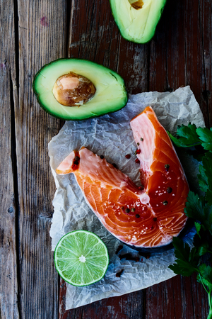 Raw salmon steak, avocado, lime and parsley on rustic wooden board - healthy food, diet or cooking concept. Top view.の写真素材