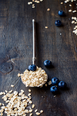 Diet Breakfast. Oats in a vintage metal spoon  and berries on wooden background - health and diet concept. Selective focus.の写真素材