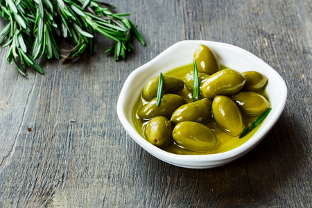 fresh green olives in a bowl of olive oil on vintage wooden texture, selective focusの写真素材