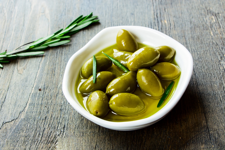 bowl of fresh green olives in olive oil on a rustic wooden texture, selective focusの写真素材
