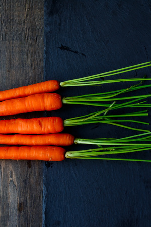 Top view of bunch of fresh carrots with green leaves over wooden background. Vegetable. Foodの写真素材