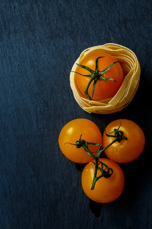 Top view of raw pasta and fresh cherry tomato over dark gray background. Copy space.の写真素材