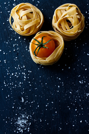 Top view of cherry tomato and raw pasta with sea salt on dark gray texture.の写真素材