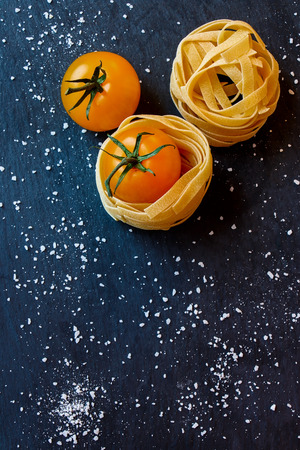 Raw pasta, cherry tomato and sea salt on dark gray background. Top view.の写真素材