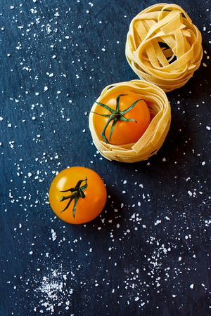 Top view of raw pasta, cherry tomato and sea salt on dark gray background.の写真素材
