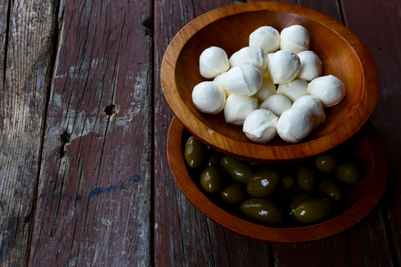 Mozzarella cheese and green olives in wood bowl over vintage wooden textureの写真素材